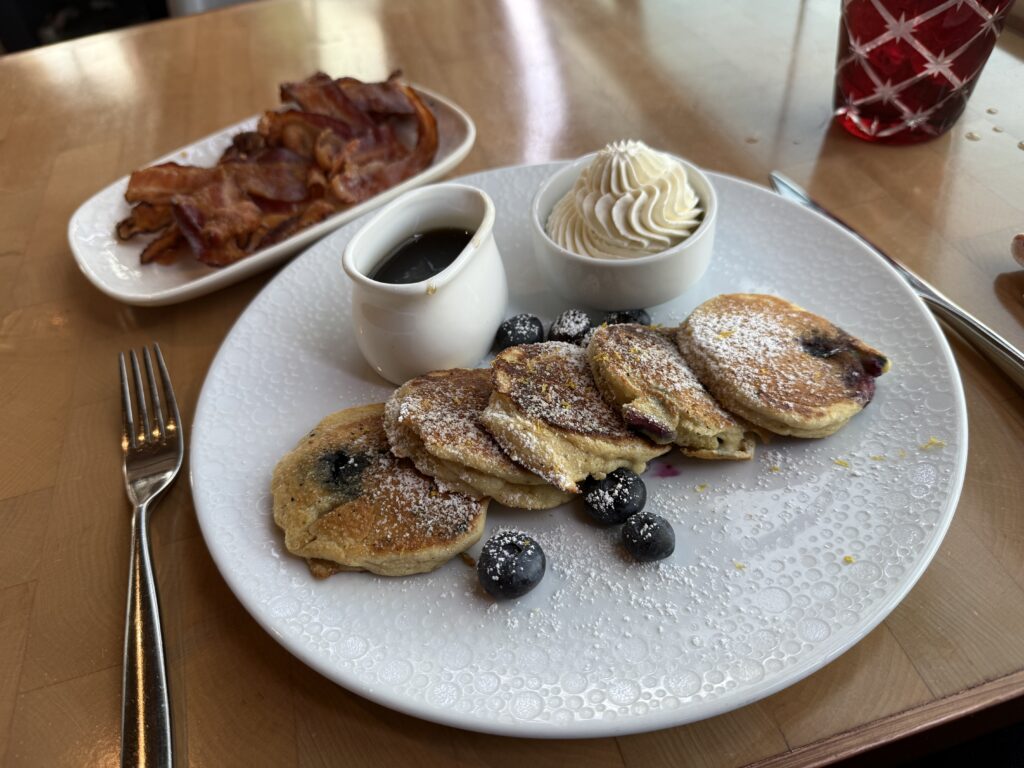 A plate of blueberry pancakes with a smaller plate piled with bacon. 