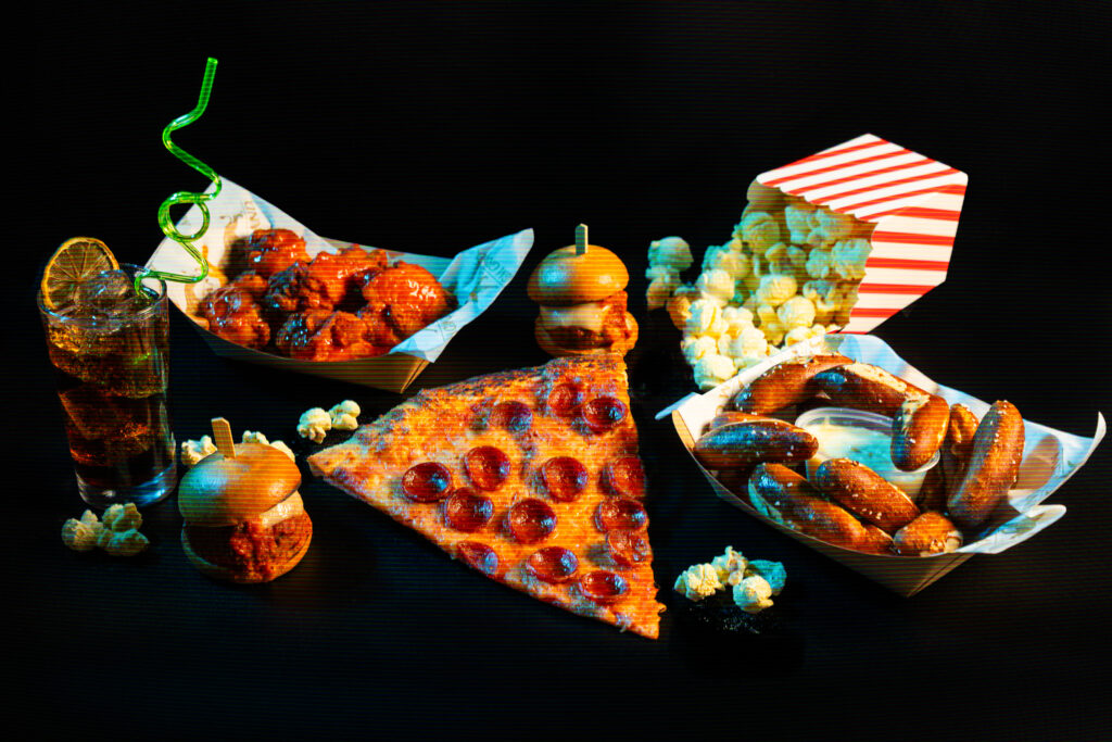 A collection of snack foods like pizza, wings, and a giant pretzel set on a black background. 