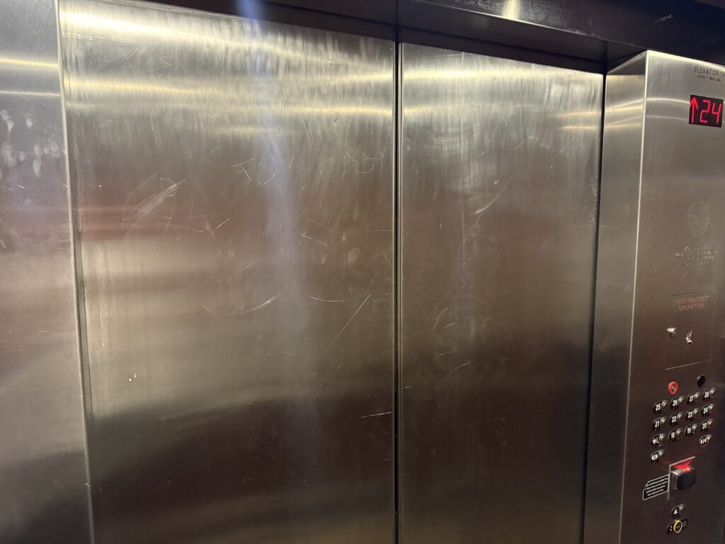 Elevator interior with scratched stainless steel doors and a right-side control panel displaying floor 24.