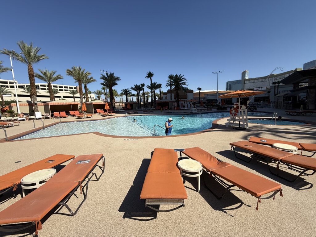 An outdoor pool, 50% of which is in the shade with orange loungers in the foreground. 