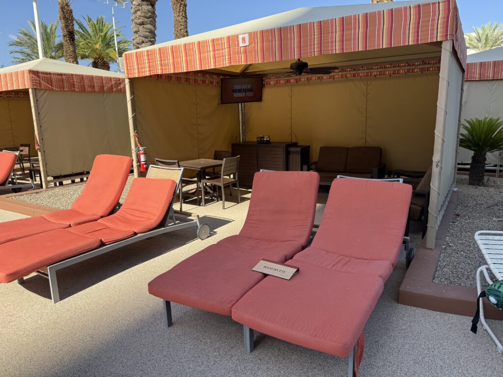A pool cabana with 4 loungers, a tv, and a fridge. 