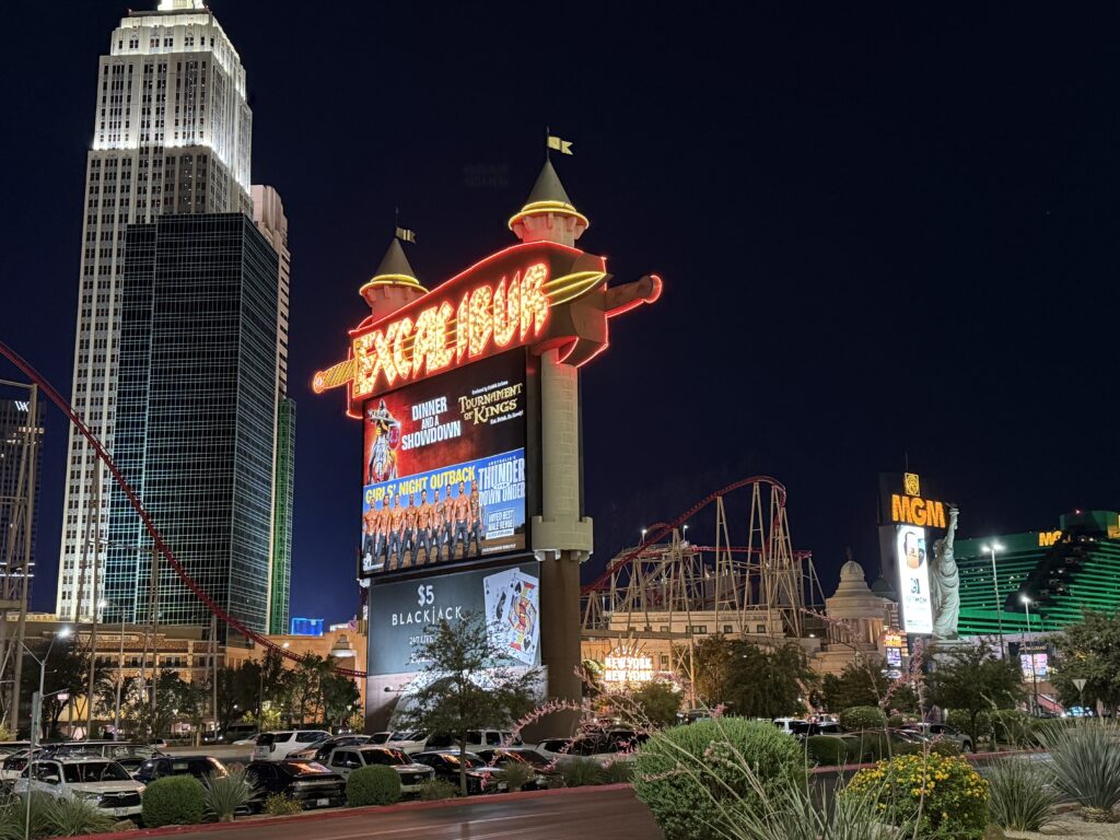 Excalibur's sign at night, illuminated with NYNY in the background. 