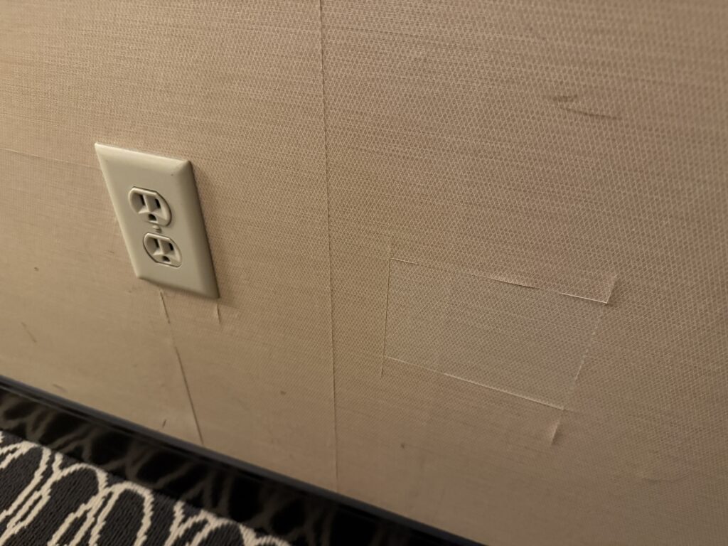 A square of patched wallpaper on a wall next to an outlet.