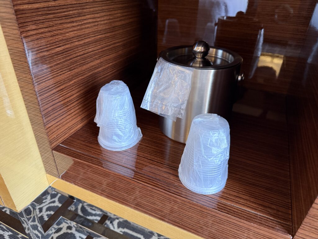 Metal stainless container with a rounded lid knob on a wooden shelf, with several translucent plastic bags wrapped around its base.