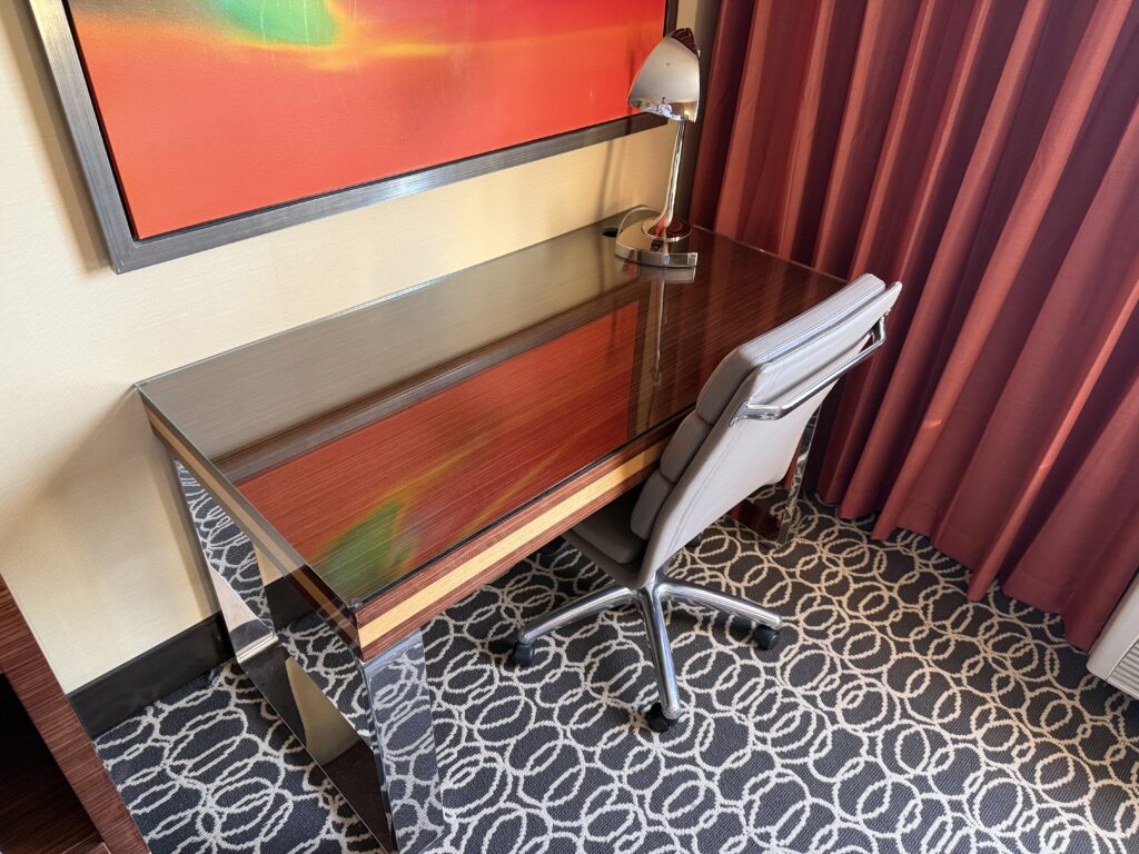 Glass topped work desk with a rolling chair. A painting is hanging above it. 