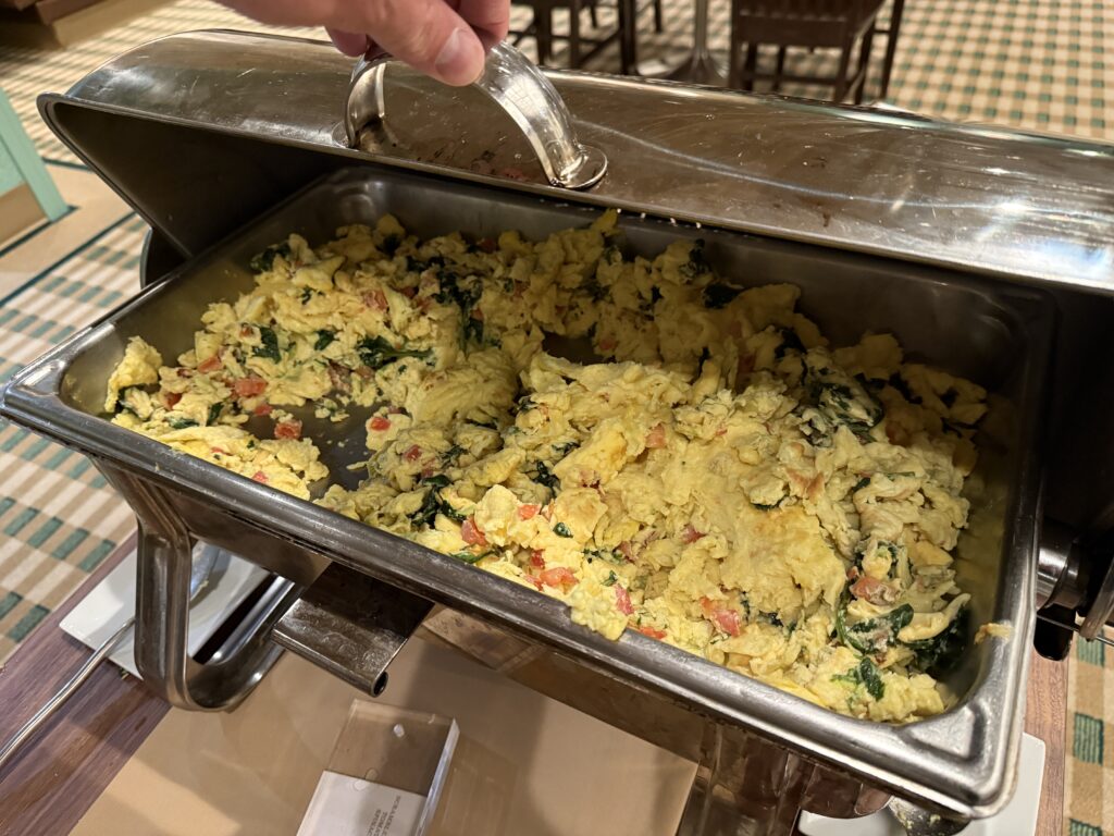 A warming tray stocked with scrambled eggs that had diced tomatoes and spinach mixed in. 