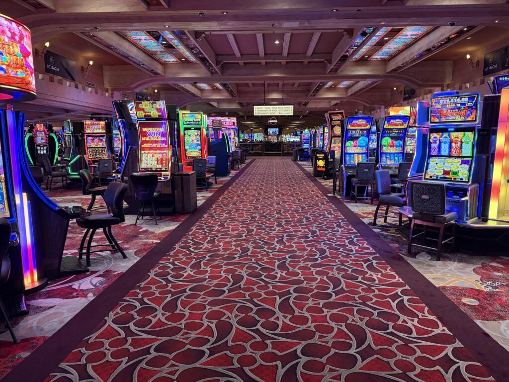 A walkway cutting through Excalibur's casino floor, flanked by rows of illuminated slot machines on either side. 