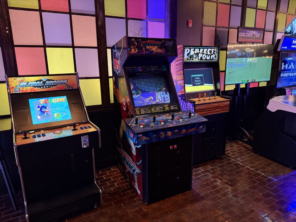 Row of vintage arcade machines with colorful side panels in a dimly lit arcade room.
