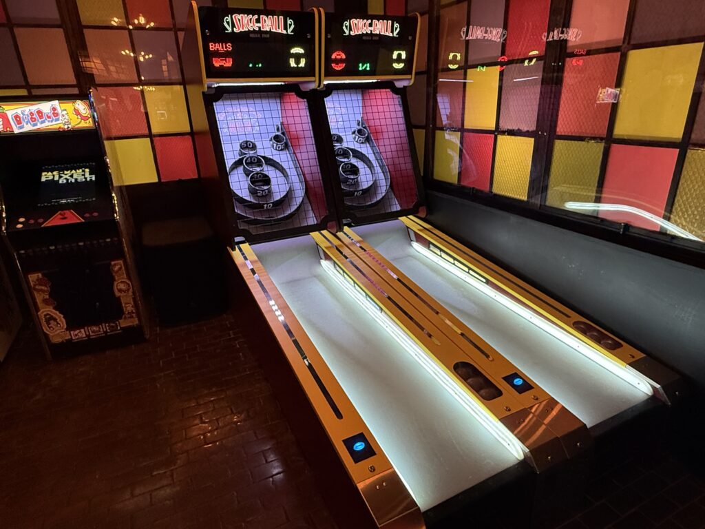 Arcade skee-ball lanes with glowing scoreboards and colorful wall panels in red, yellow, and orange hues.