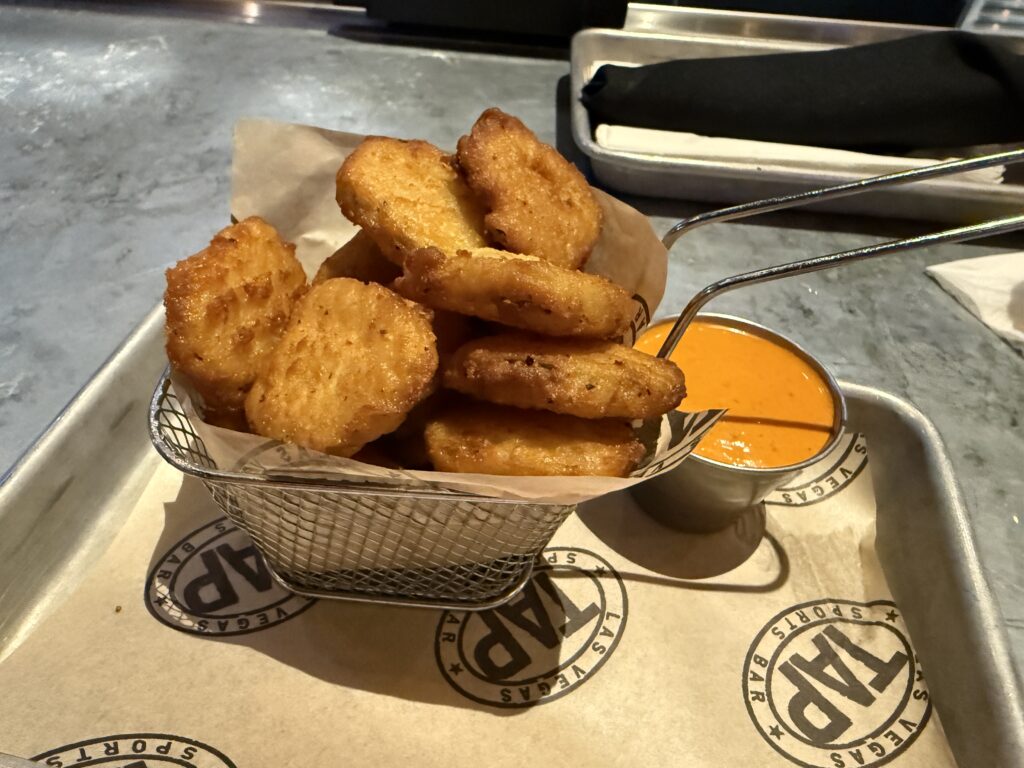 Basket of fried pickles next to a chipoltle ranch sauce. 