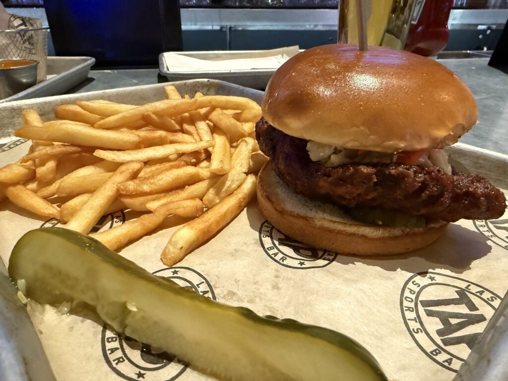 Hot Chicken Sandwich, a pile of french fries, and a pickle spear on a tray. 