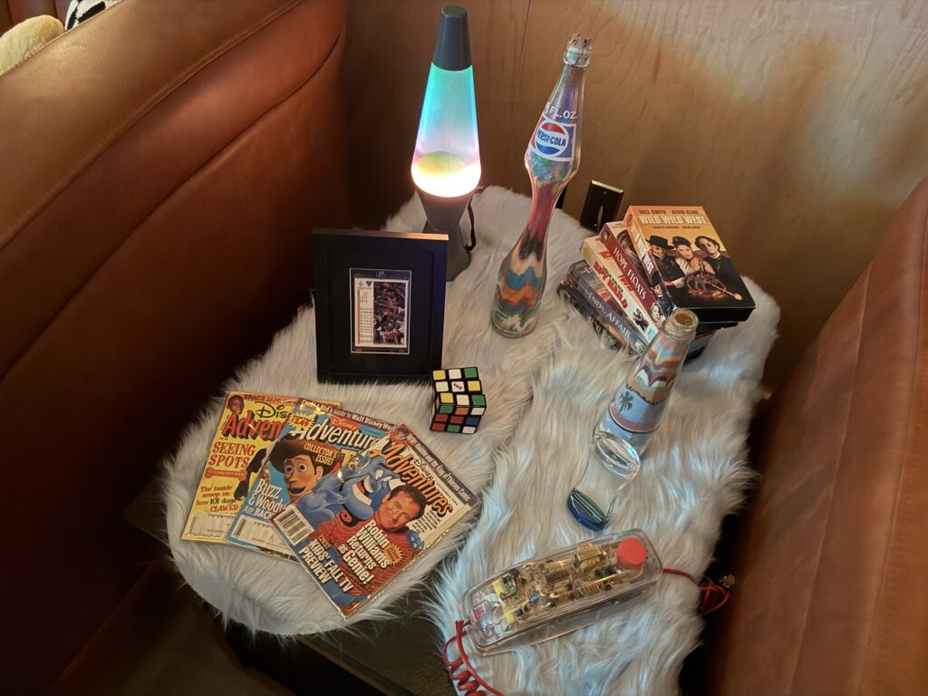 A table full of 90s items like a lava lamp, magazines, a rubrik cube, and more. 