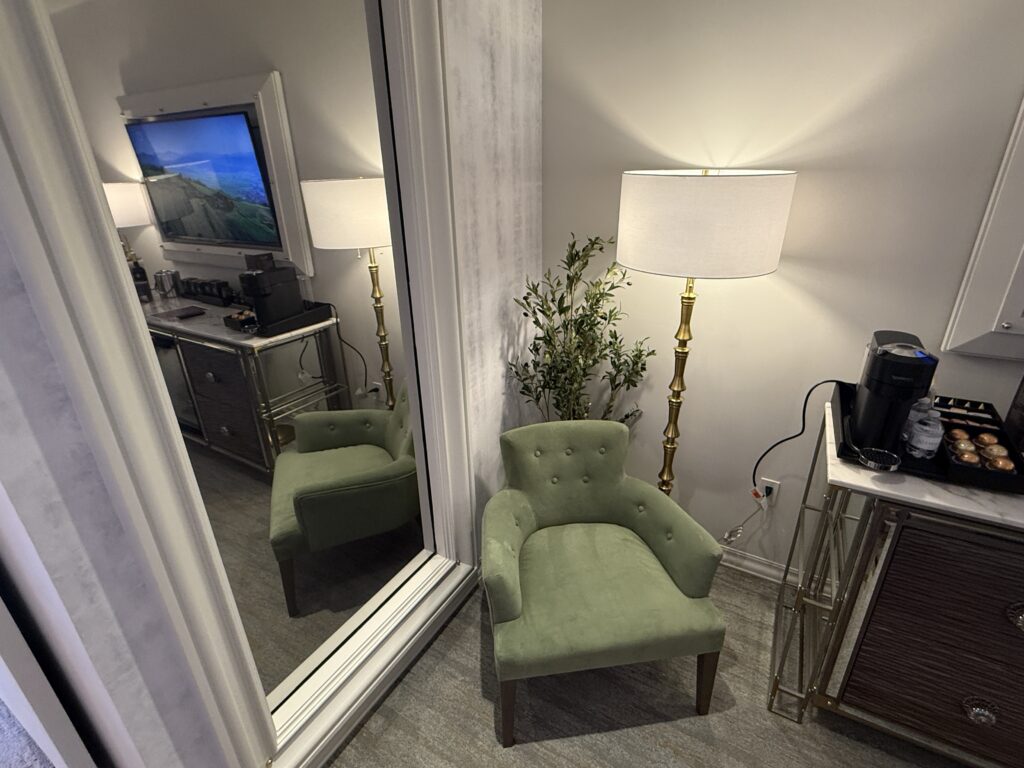 A green chair, under a lamp in front of a huge 2 way mirror. 