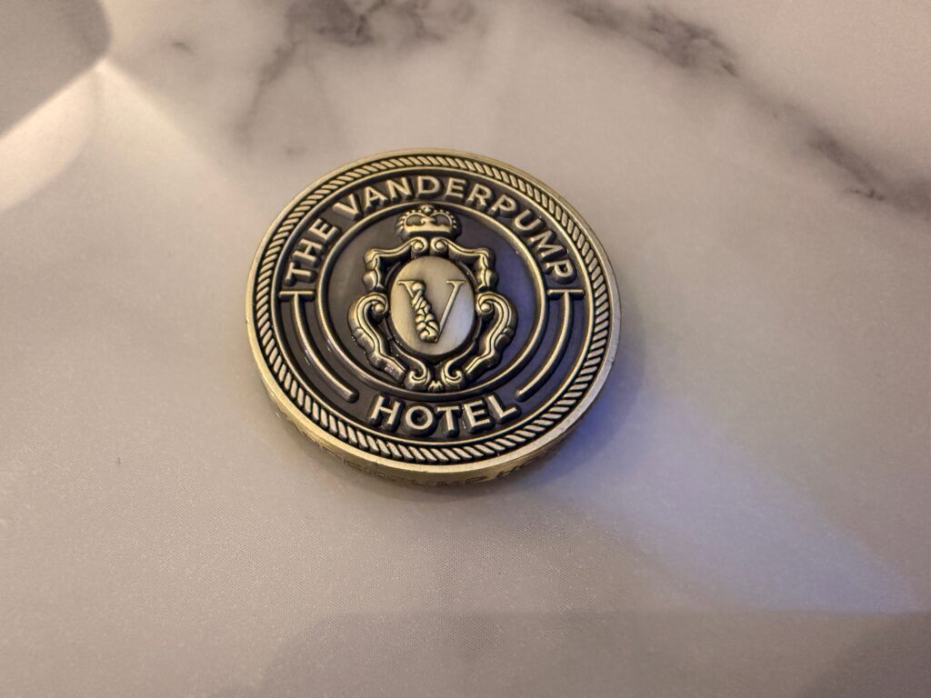 A metal token that says "The Vanderpump Hotel" laying on a marble countertop. 