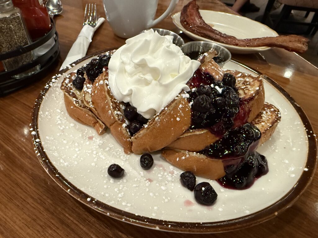 A pate with blueberry French toast, topped with blueberries and a huge blob of whipped cream.