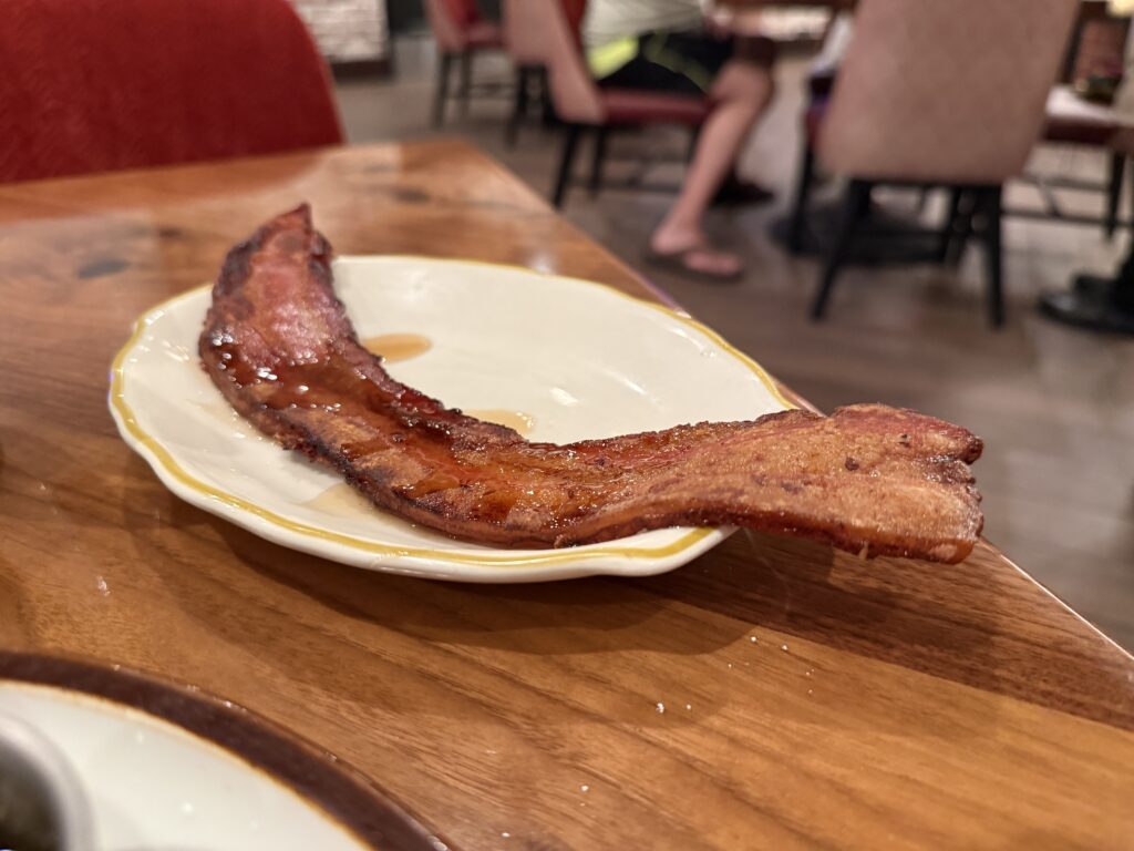A thick slice of bacon, hanging off the sides of a small plate.
