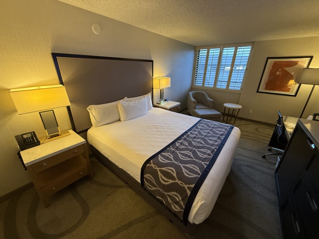 Wide angle of the room, which shows a king bed with a window covered by shutters in the background.