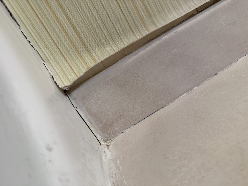 Peeling wallpaper near the baseboard in thebathroom.