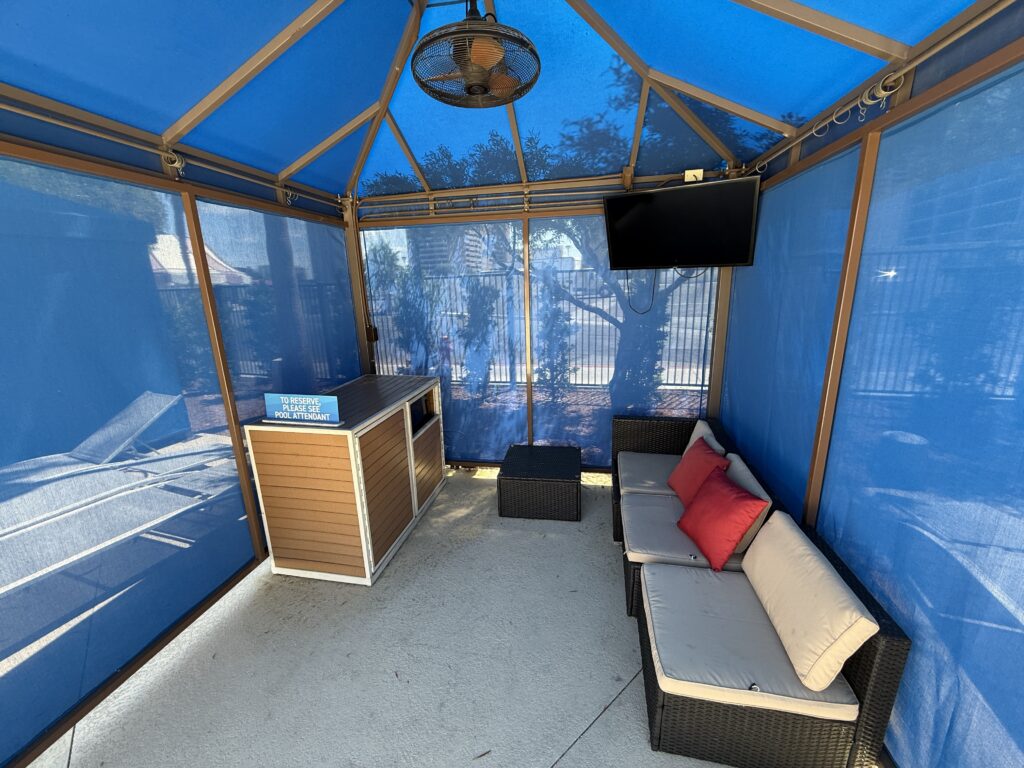 Interior of a pool cabana with a couch, tv, and fan.