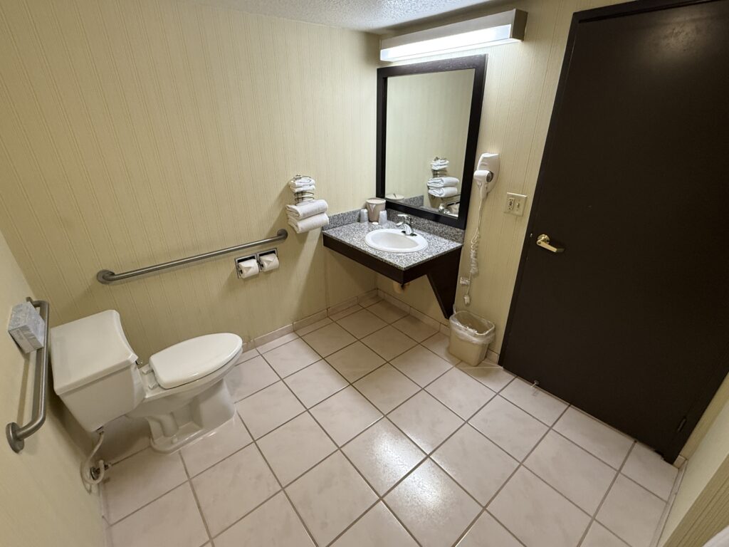 Wide angle shot of the bathroom, which has a toilet pointed to a single sink vanity.