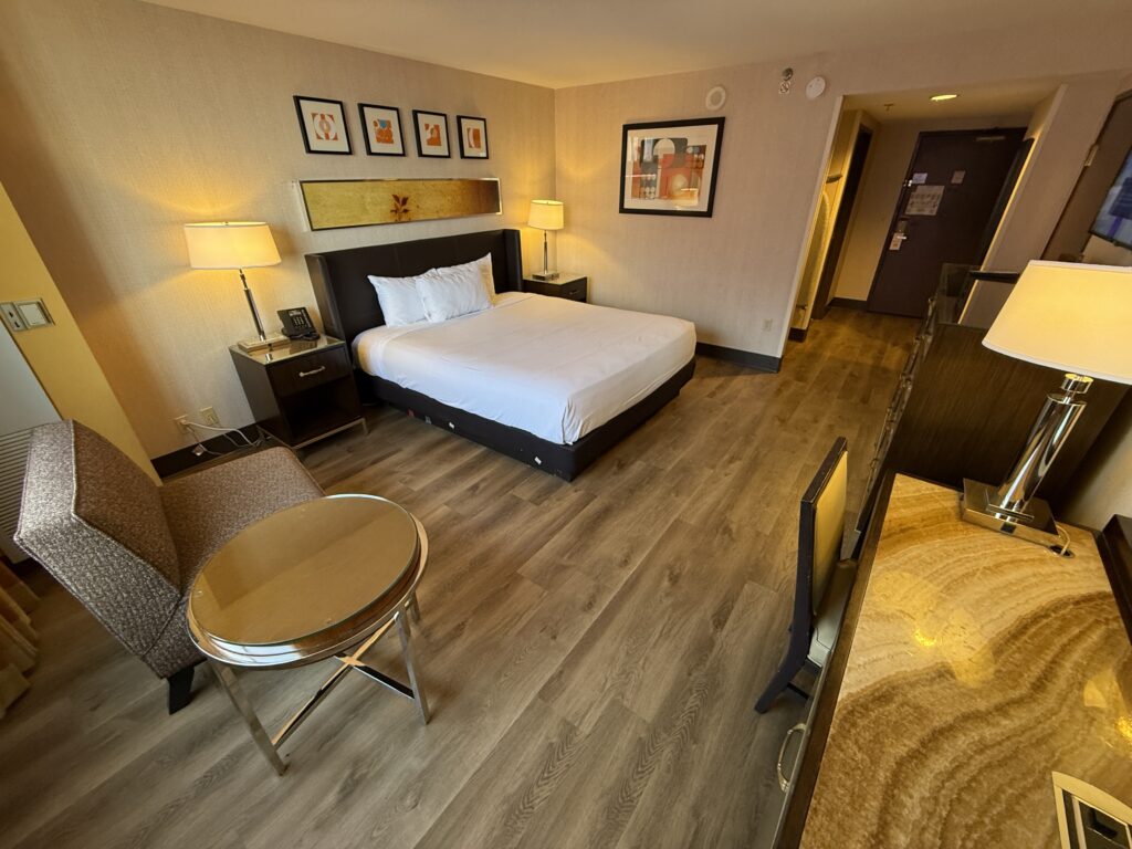 Another Angle of the room which shows a chair and table in the foreground, and the bed and entryway in the background.