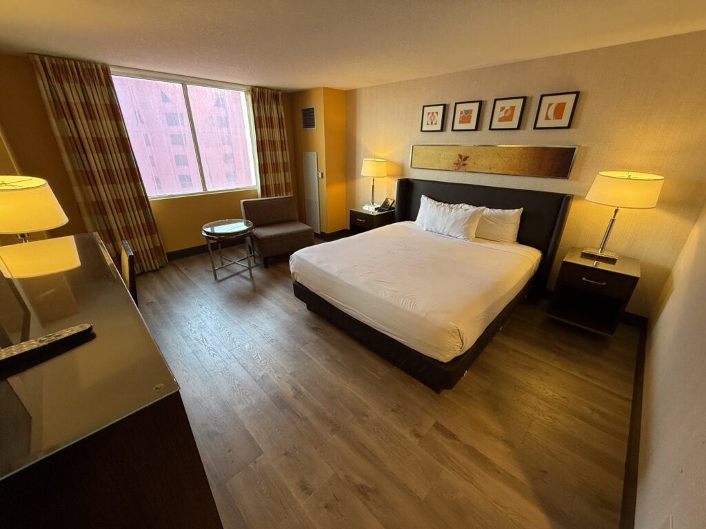 A wide angle photo of the room, with a king bed and window in the background.