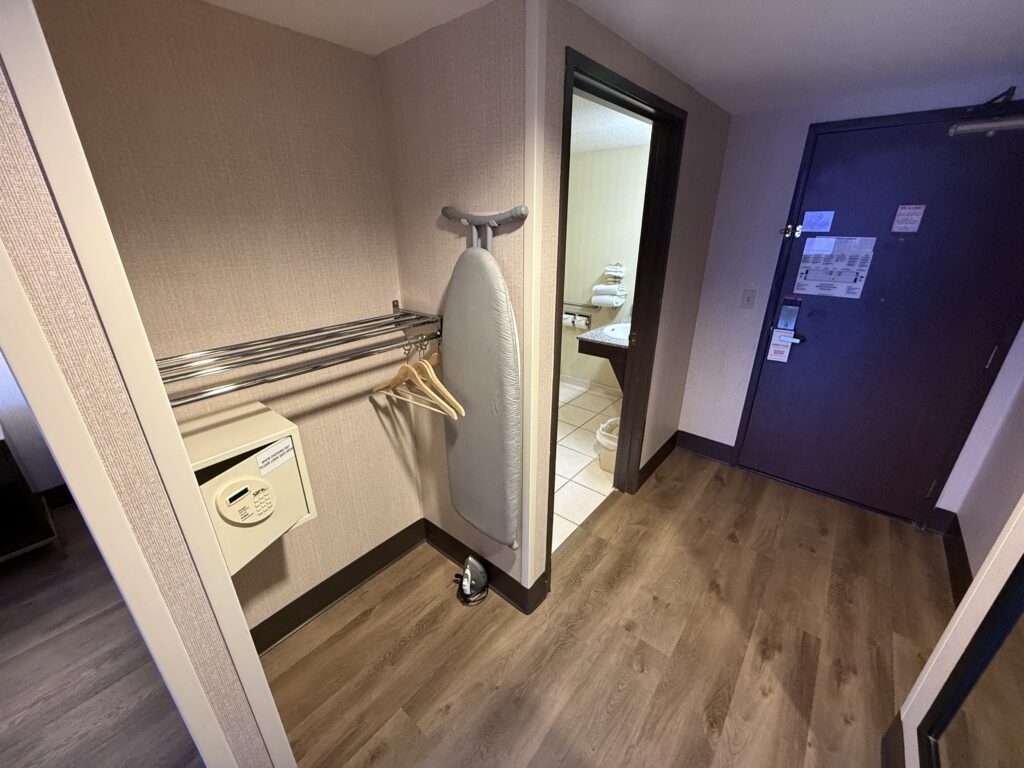 Hotel closet stocked with an iron, ironing board, and a clothing rack.