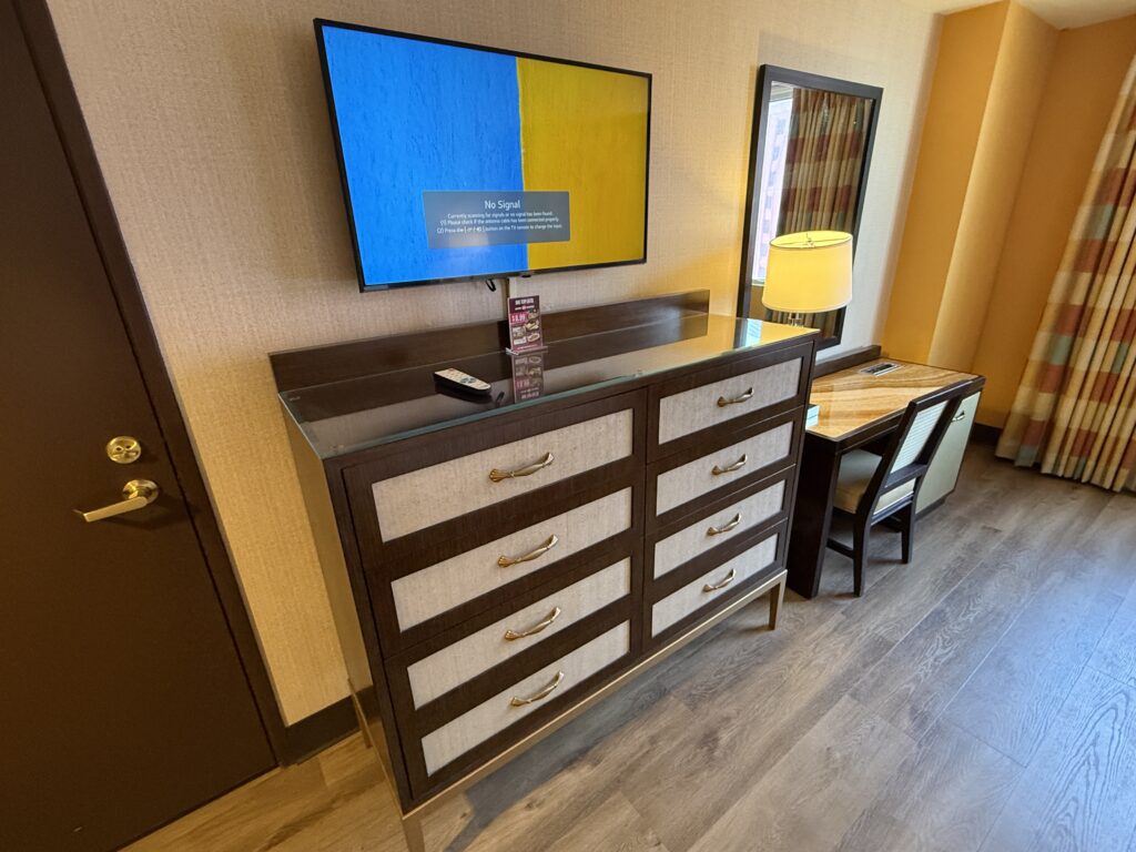A TV mounted on a wall above an 8 drawer dresser.