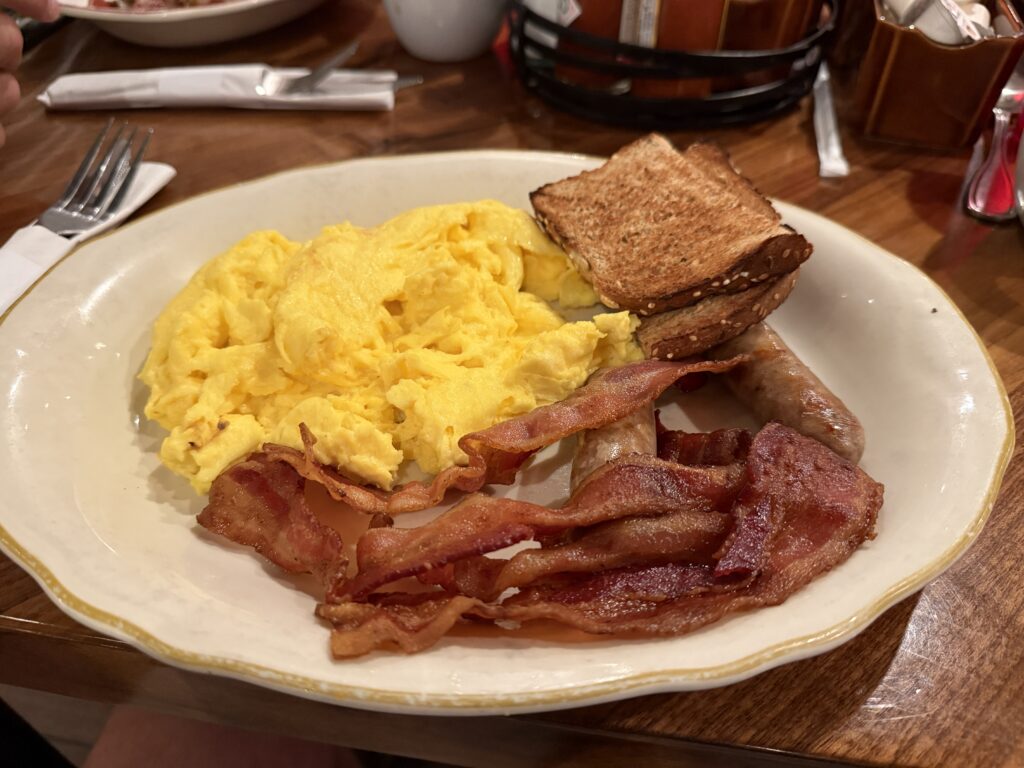 A plate piled with scrambled eggs, bacon, sausage and toast. 