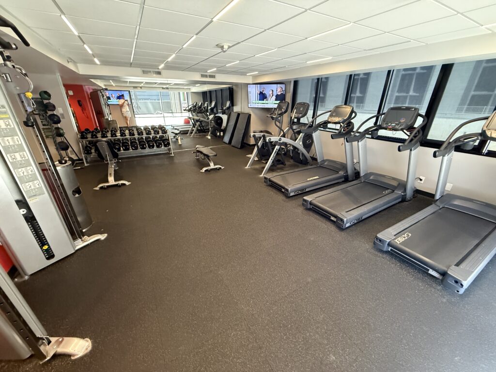 A gym, with a row of treadmills to the right and a rack of weights in the background. 