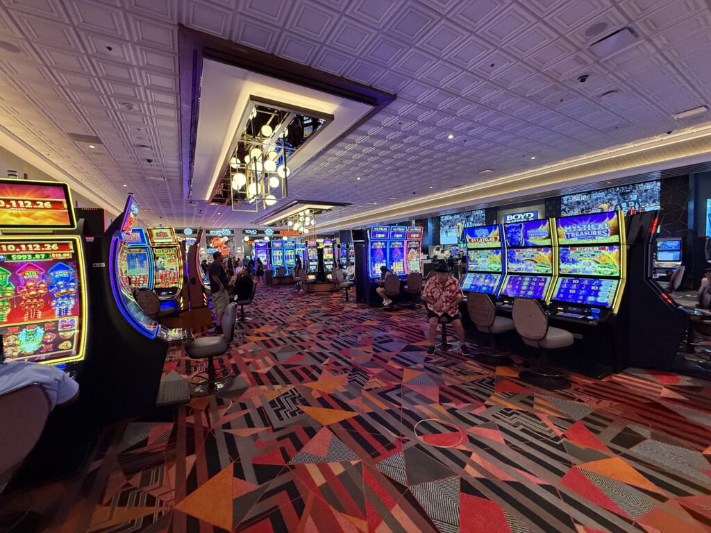 The casino floor, which has a lot of slot machines and a decorative light fixture from the ceiling. 
