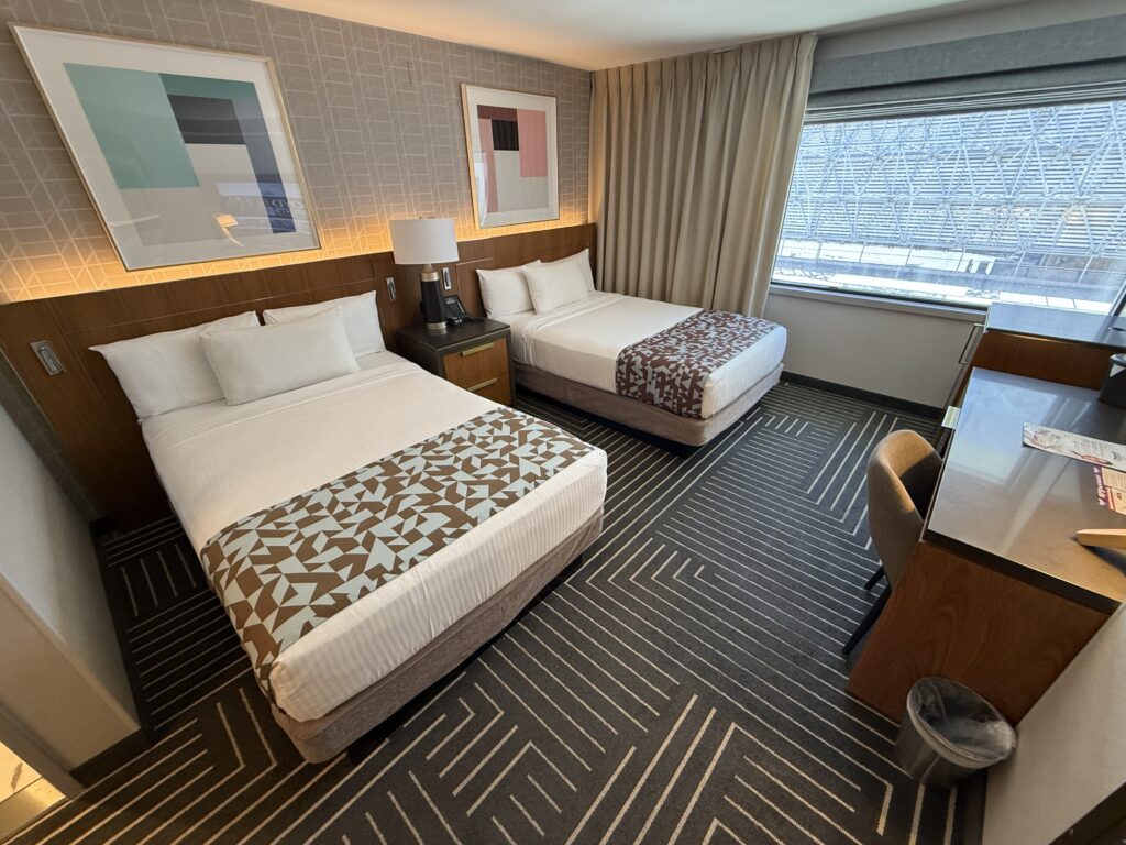A wide angle view of the room, which is 2 beds against a wall and a window to the right. 