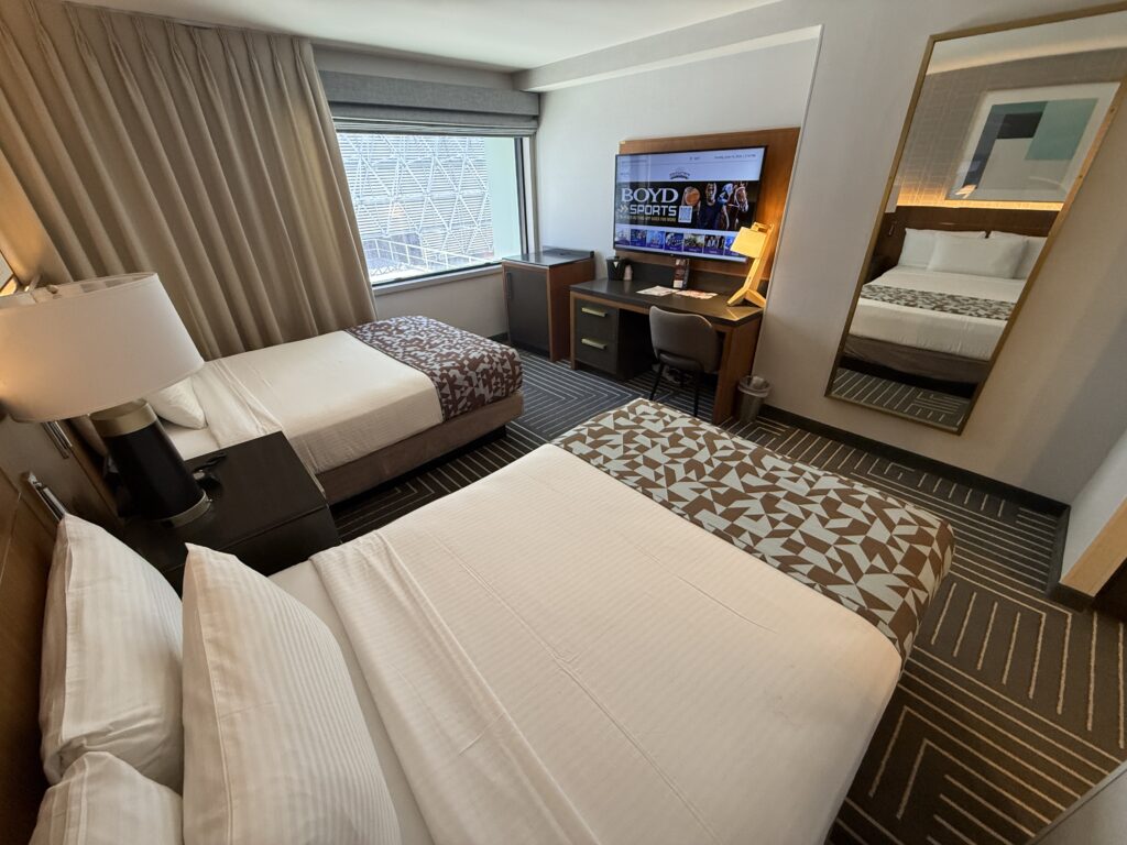 Hotel room with two double beds pointed at the TV with the window in the background. 