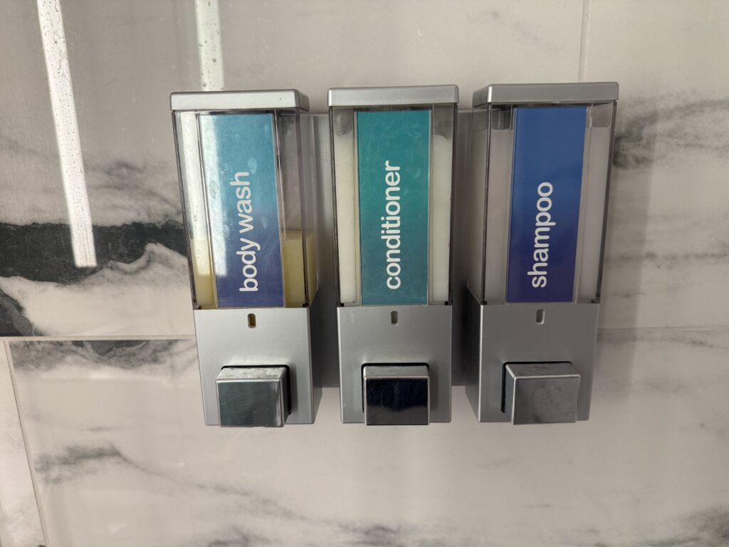 Three wall-mounted liquid dispensers labeled body wash, conditioner, and shampoo.