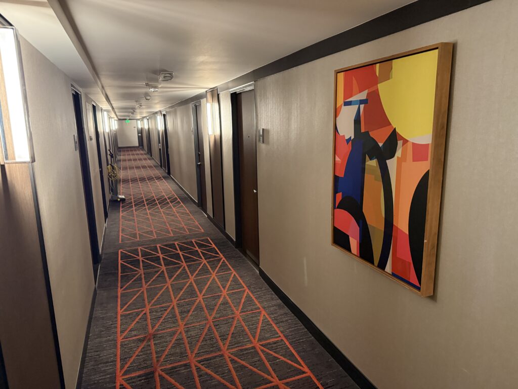 Hotel hallway which is well lit, with bright abstract artwork on the wall. 
