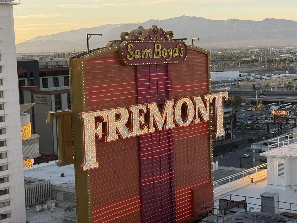 Sam Boyd's neon sign with Fremont letters, set against a desert cityscape and distant mountains at dusk.