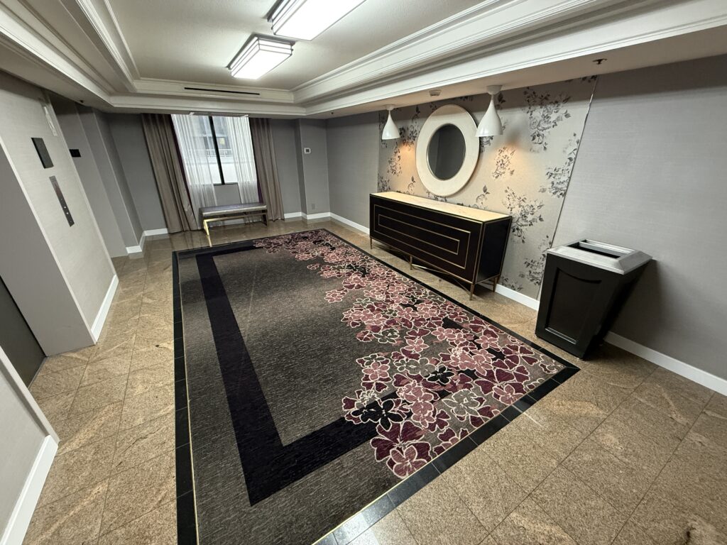 A hotel elevator lobby with floral pattered carpet, good lighting, and a generally nice look. 