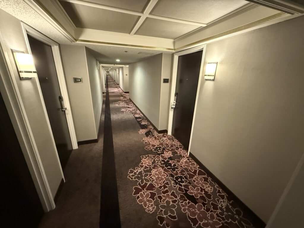 A hotel hallway with floral themed carpeting. 