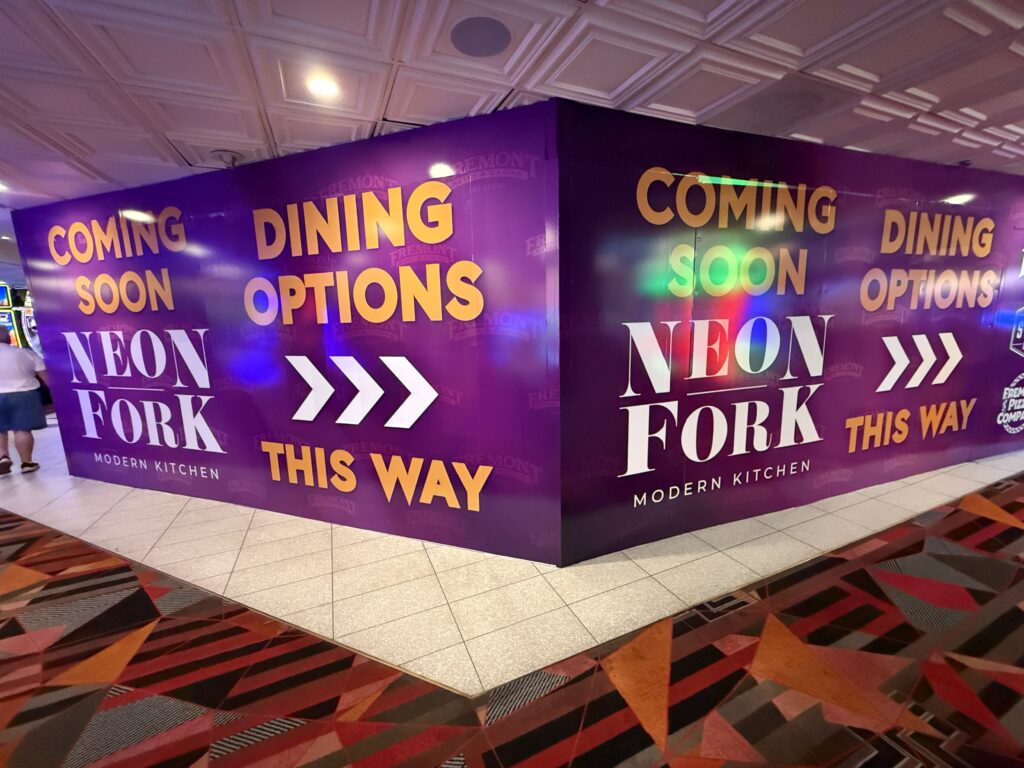Promotional wall reading 'COMING SOON DINING OPTIONS' in large yellow letters on a purple background, with 'NEON FORK Modern Kitchen' branding nearby inside a mall.