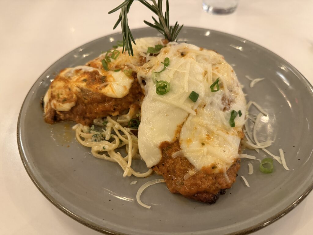 Two chicken pieces covered in melted cheese rest atop a pile of noodles.