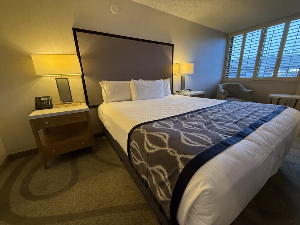 Shutters, open in the background, letting in light, with the bed in the immediate foreground.