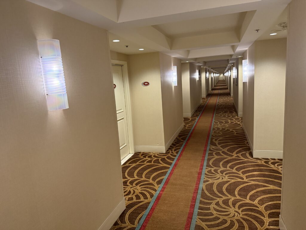 Long hotel hallway, with seashell patterned brown carpeting and great lighting.