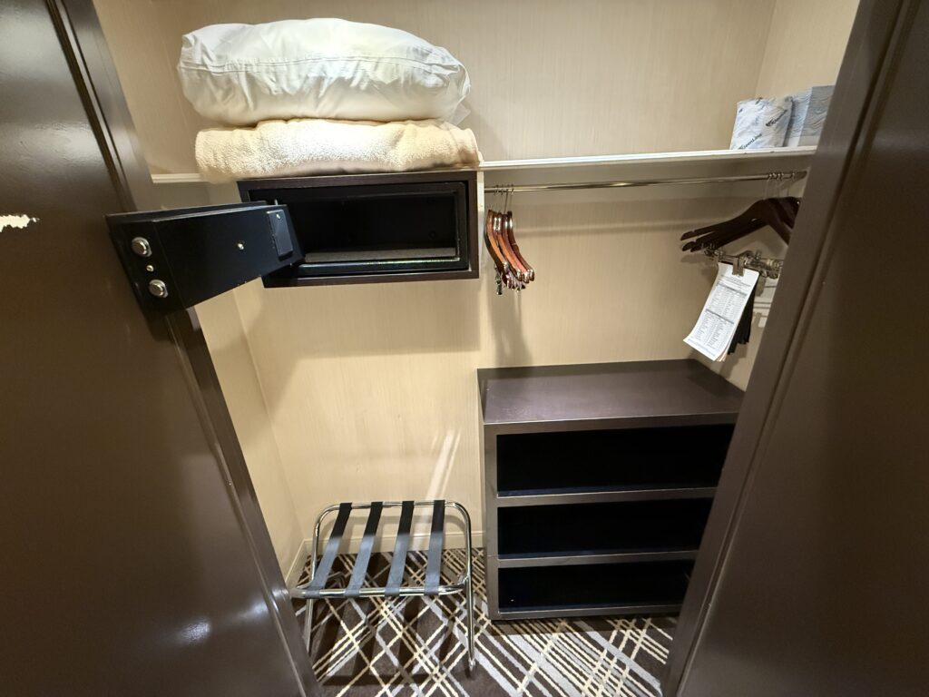 A closet stocked with a pillow, blanket, iron, ironing board, and backup toilet paper.
