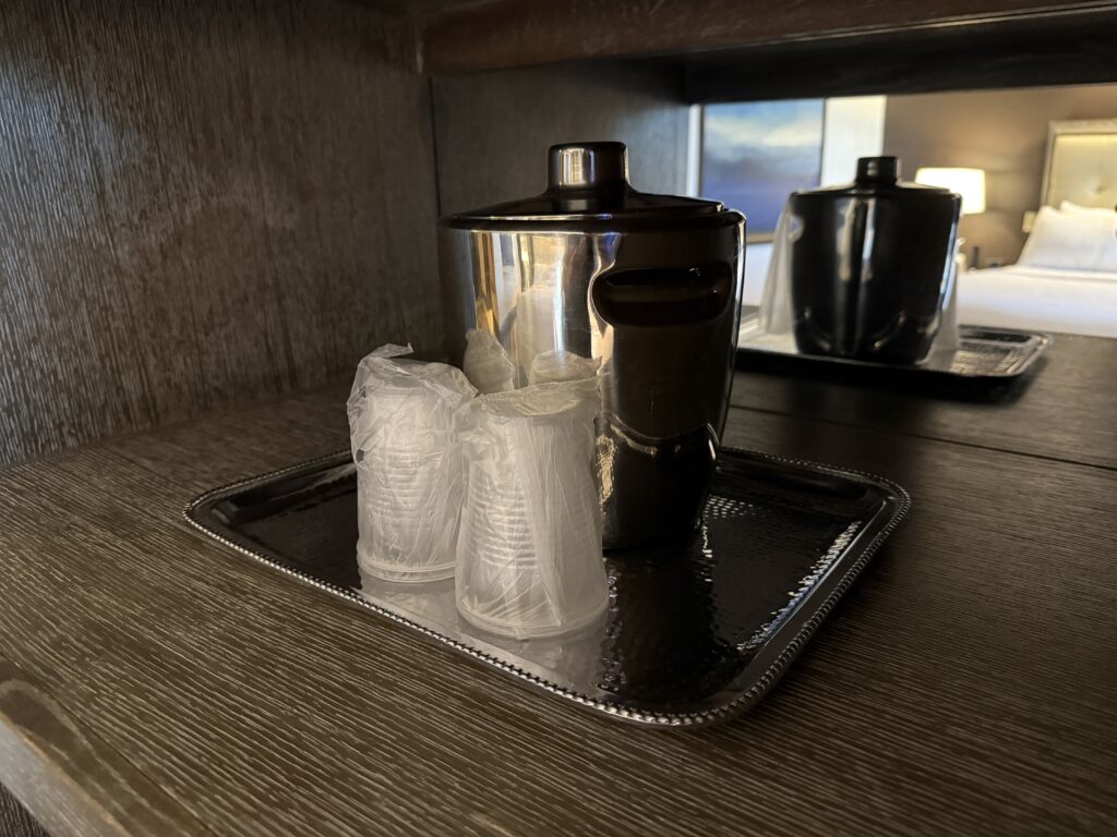 A metal ice bucket behind two stacks of clear plastic cups.