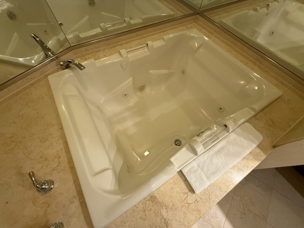 A large, white square jetted baththub from above.