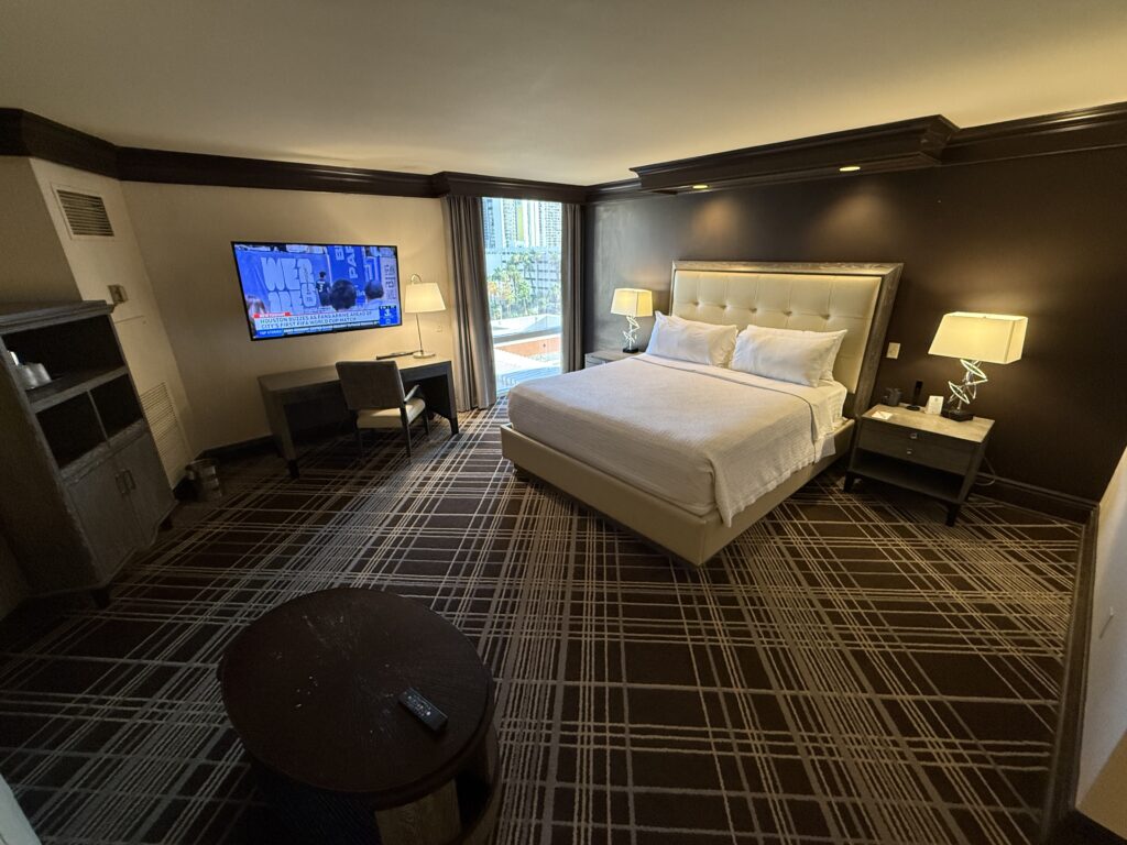 A wide angle shot of the suite, which shows a king bed with lights above illuminateing it.