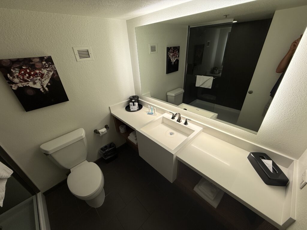 An illuminated mirror above a single sink vanity. A toilet sits to the left.