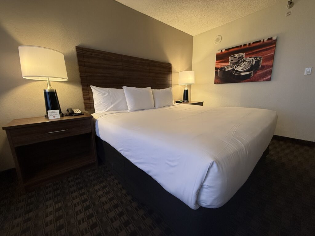 A close up of the king bed, flanked by lamps. A casino themed picture hangs above the bed.