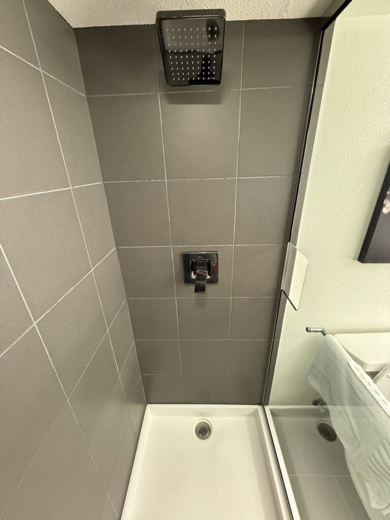 The shower, which has large gray tile walls, and a plastic bottom.
