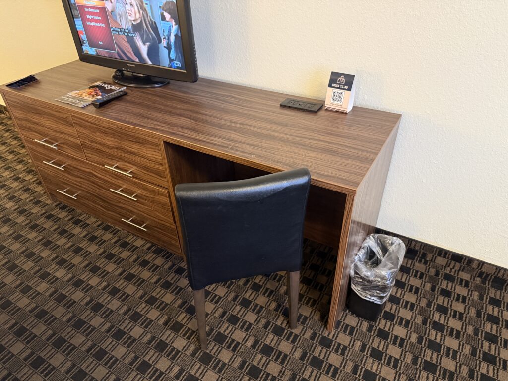 Small wooden work desk connected to the main dresser with a black faux leather chair under it.